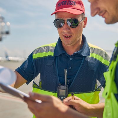 Concentrated aircraft maintenance supervisor in workwear staring at a document in his male colleague hand